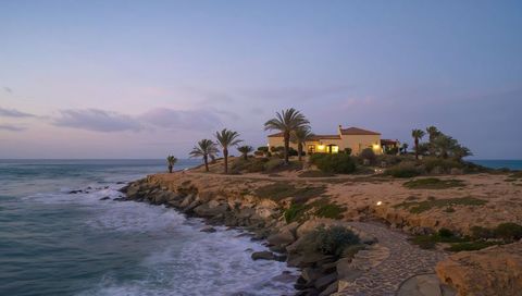 Villa perching on rocky headland with lit windows, palms and paved path at dusk