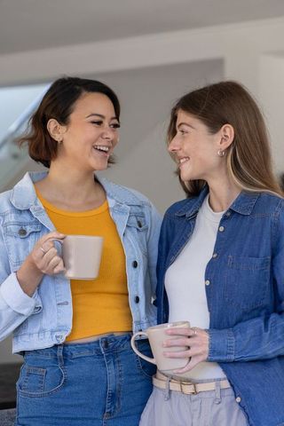 Diverse women sharing coffee and laughing in modern kitchen, casual friendship