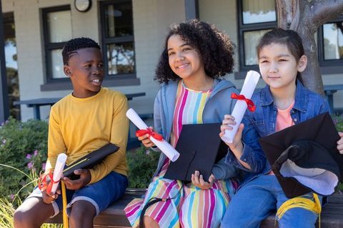 Multicultural kids celebrating kindergarten graduation outdoors with diplomas and caps