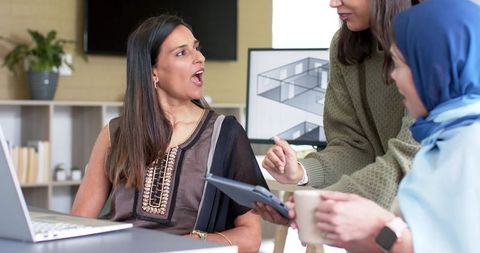 Diverse female team collaborating at desk with laptop tablet and architectural floorplan