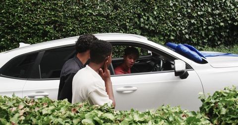 Friends talking beside white hatchback with blue cushions on hood, candid curbside conversation