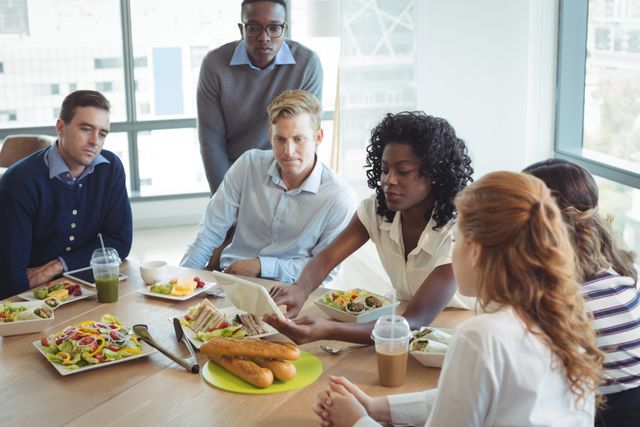 Diverse group of business colleagues having a serious discussion while sitting around a breakfast table in an office cafeteria. Ideal for use in articles or presentations about teamwork, corporate culture, office environments, and business meetings. Can also be used in promotional materials for corporate training, team-building activities, and workplace diversity initiatives.