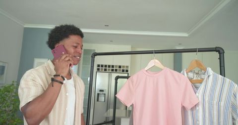Young african american man calling while arranging shirts on clothing rack in kitchen
