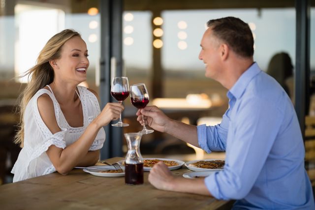 Couple enjoying a romantic meal at a restaurant, toasting with wine glasses. Ideal for use in advertisements for restaurants, romantic getaways, wine promotions, or lifestyle blogs focused on relationships and dining experiences.