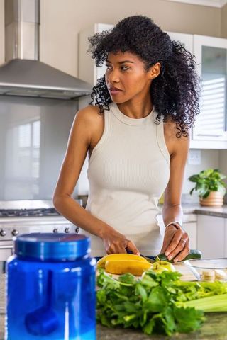 African american woman preparing fresh vegetables in sunny kitchen chopping cucumber and herbs