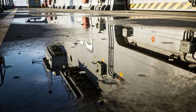 Reflecting ship deck showing industrial pipes, electrical boxes and hazard safety stripe
