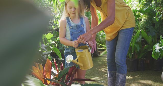 Happy caucasian mother and daughter watering plants in sunny garden. Family, nature, gardening and hobbies.