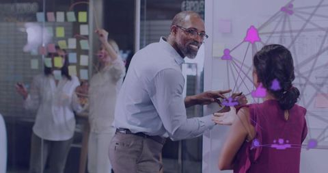 Mature professional guiding team through network planning on glass whiteboard during brainstorming