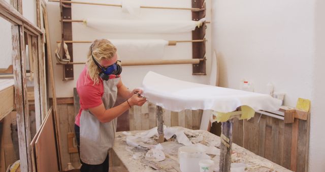 An artisan wearing a mask and working in a workshop, preparing a table surface with precision. Suitable for illustrating craftsmanship, woodworking, handcrafted furniture, professional work environments, and DIY projects.