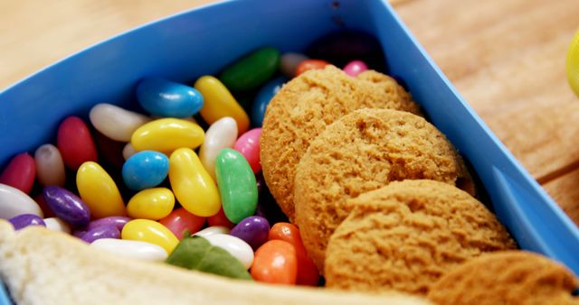 A vibrant selection of colorful jelly beans and golden-brown cookies are presented in a blue container, with copy space. The assortment of sweets offers a visual treat, suggesting a setting for a casual snack or a festive occasion.