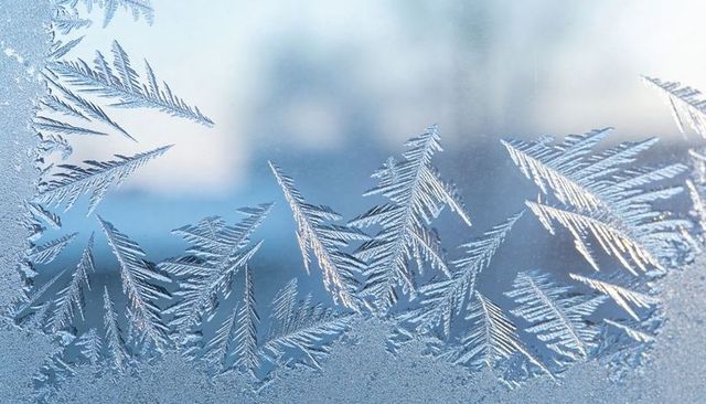 Frost feather patterns on window glass, delicate ice crystals and winter texture