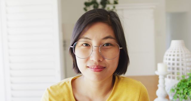 Smiling woman with short hair wearing round glasses and yellow shirt in bright, naturally lit room. Perfect for lifestyle, casual moments, personal blogs, and articles on everyday life. Emphasizes simplicity and positive mood.