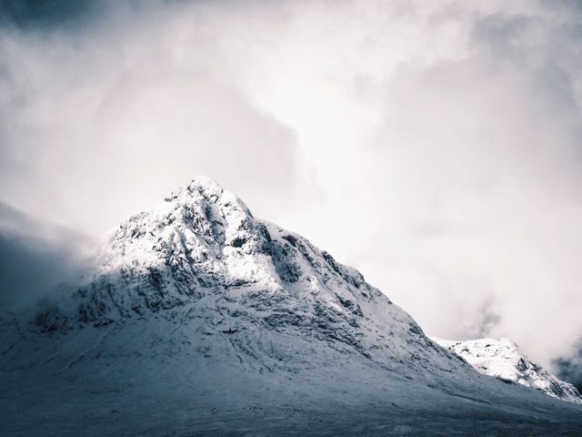 Snow-covered mountain peak under a cloudy, overcast sky. The scene projects a sense of cold, harsh beauty, emphasizing the raw, untamed wilderness. Ideal for use in travel magazines, outdoor adventure promotions, or winter-themed content.