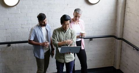 Diverse Coworkers Collaborating on Laptop in Office Stairwell