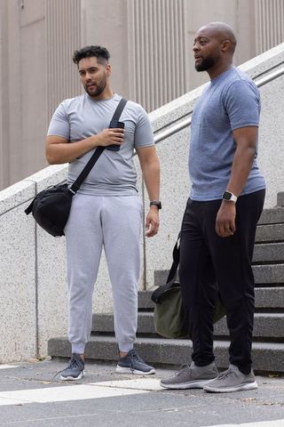 African american men standing on urban steps holding duffel bags and smartphone