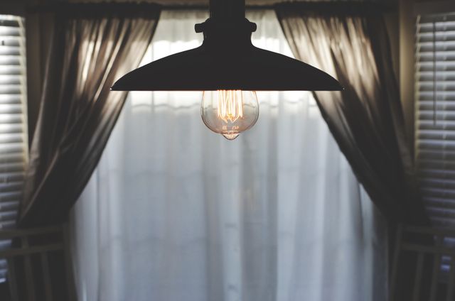 Beautiful vintage hanging light bulb casting glow in minimalist room with curtains and blinds. Perfect for articles on interior design, minimalist decor, and home renovation ideas. Ideal for blog posts, lifestyle magazines, or social media content.
