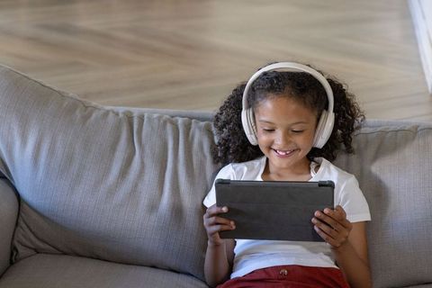 School-age african american girl enjoying tablet with headphones on cozy sofa at home