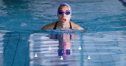 Female athlete practicing breaststroke in indoor pool wearing cap and goggles, training
