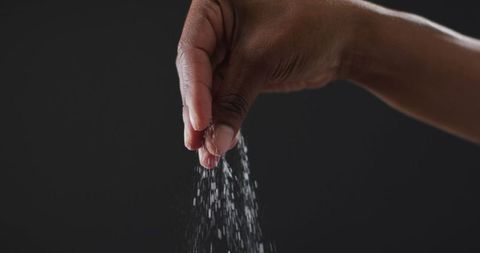 Hand Sprinkling Salt Against Dark Background