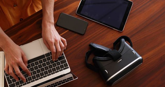 Person Working on Laptop with VR Headset, Tablet, and Smartphone on Wooden Desk - Download Free Stock Images Pikwizard.com