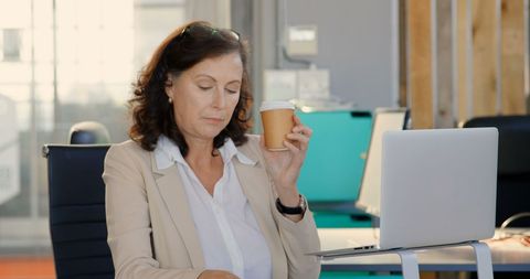 Businesswoman Enjoying Coffee and Using Laptop in Office