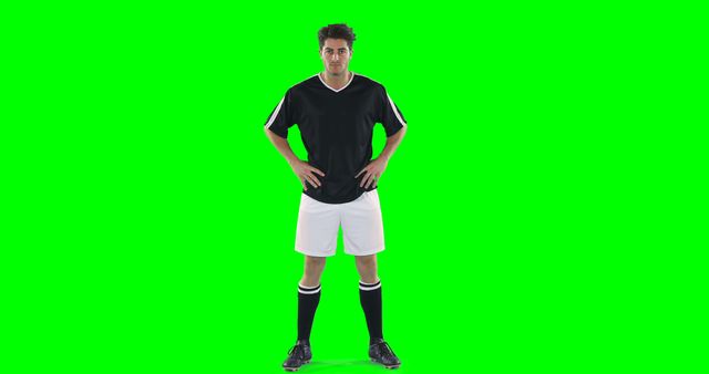 A confident soccer player in black and white sportswear posing with hands on hips against a green screen background. Useful for sports promotions, fitness campaigns, training materials, or editing in sports-themed videos.