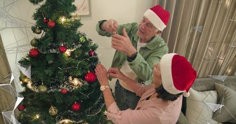Senior couple decorating christmas tree wearing santa hats sharing cozy holiday moment