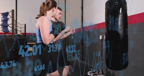 Boxing pair training with digital performance overlay punching heavy bag in gym