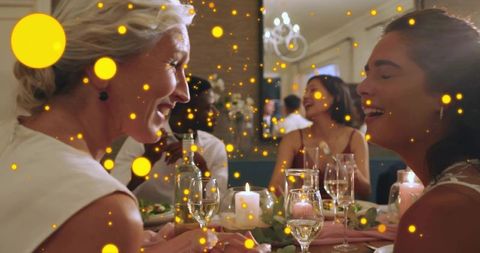 Laughing women sharing candlelit dinner with wine during intimate friends celebration night