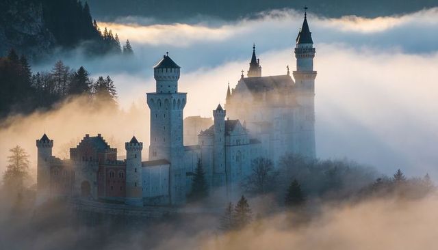 Fairytale castle rising through morning fog over misty alpine valley with sunlit turrets