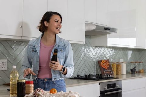 African woman smiling and holding bottle in modern bright kitchen preparing pantry items