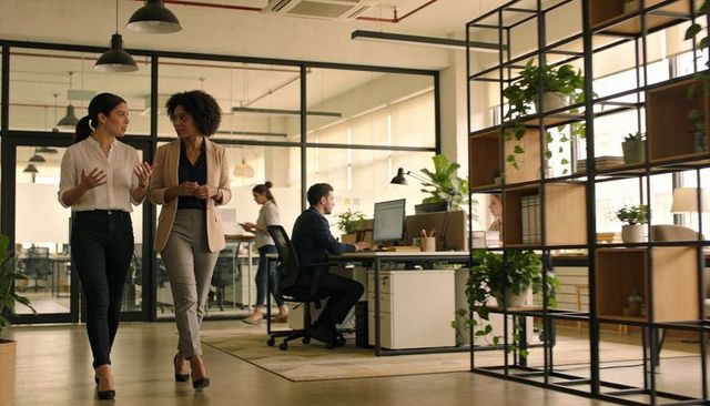 Two female colleagues walking and discussing in modern biophilic open-plan office