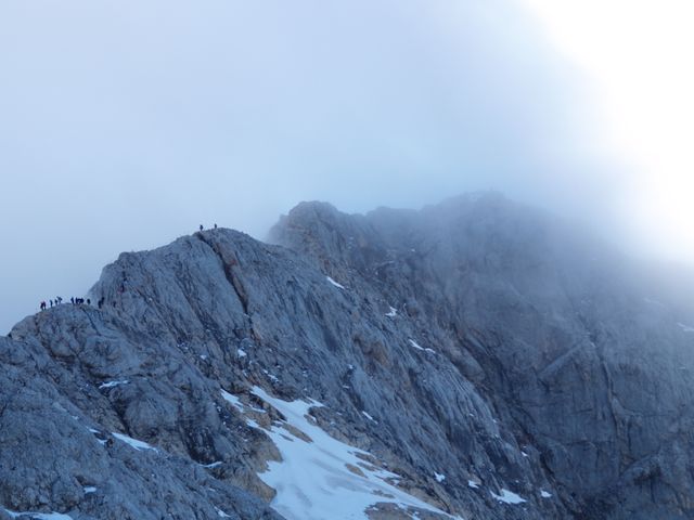 Group of climbers navigating a foggy, rugged mountain peak. Ideal for use in travel brochures, outdoor adventure campaigns, and articles about hiking and exploration.