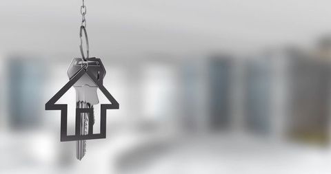 Chrome house keyring holding single key over blurred modern interior for real estate
