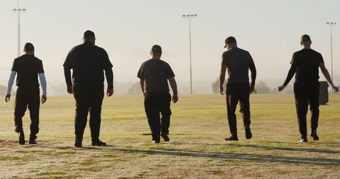 Five male teammates walking across dew-covered sports field at sunrise