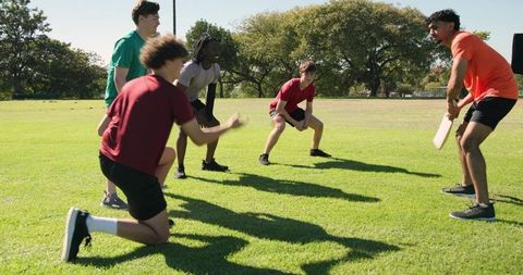 Diverse men practicing cricket fielding drill on sunny park lawn