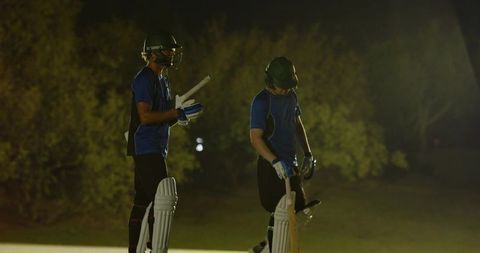 Night cricket teammates high-fiving while switching strike under stadium floodlights
