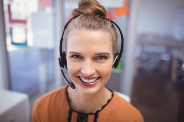 This image features a smiling customer service representative wearing a headset in an office environment. Ideal for use in business websites, customer support materials, training manuals, and promotional content highlighting professional and friendly customer service.