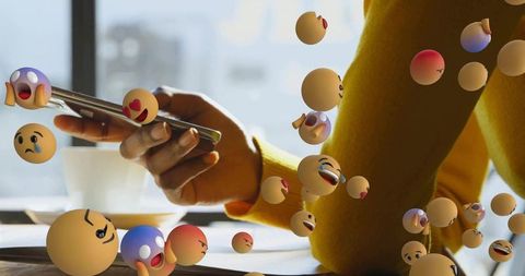 Person scrolling smartphone in modern workspace with emojis swirling