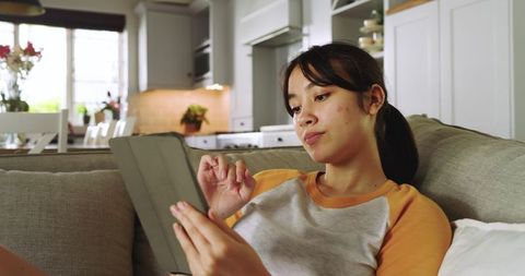 Young Woman Relaxing on Sofa Using Tablet in Modern Kitchen
