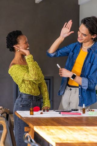 Diverse friends high-fiving testing makeup on wooden table sunlit home beauty collaboration