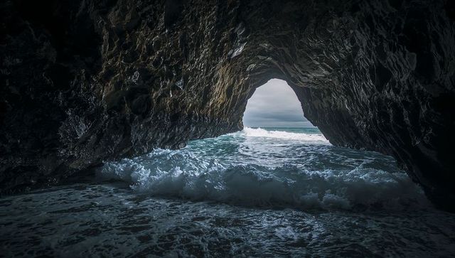 Ocean cave arch crashing waves filling grotto with wet rock walls dramatic coastal view