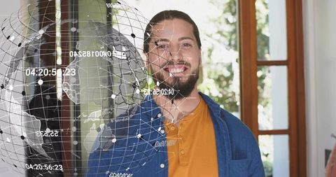 Smiling man standing by glass door with holographic globe overlaying global network