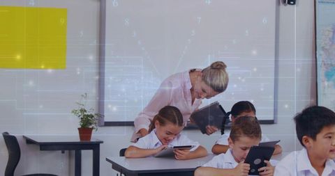 Teacher leaning over student guiding tablet learning in modern classroom with whiteboard