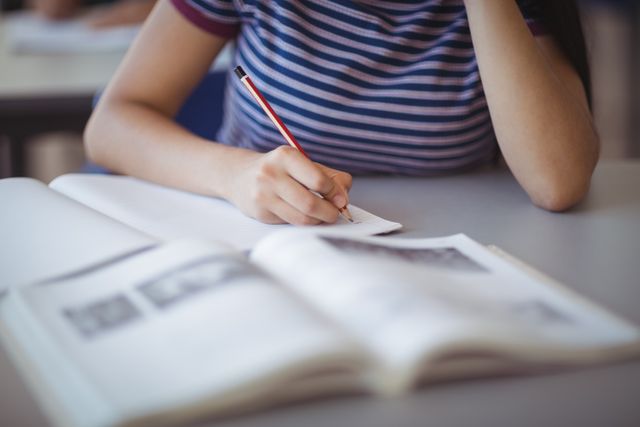 Student writing notes in a classroom setting, focusing on her work. Ideal for educational content, school-related articles, study tips, and academic resources.