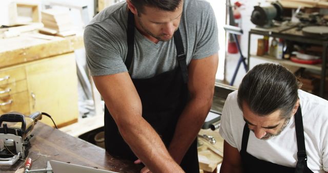 Two carpenters are collaborating on a woodworking project. One is explaining something to the other, demonstrating teamwork and skill-sharing in a workshop. Ideal for showcasing craft, design, teamwork, carpentry skills, and manufacturing processes. Useful for articles or content related to woodworking, small business, craftsmanship, or occupational trades.