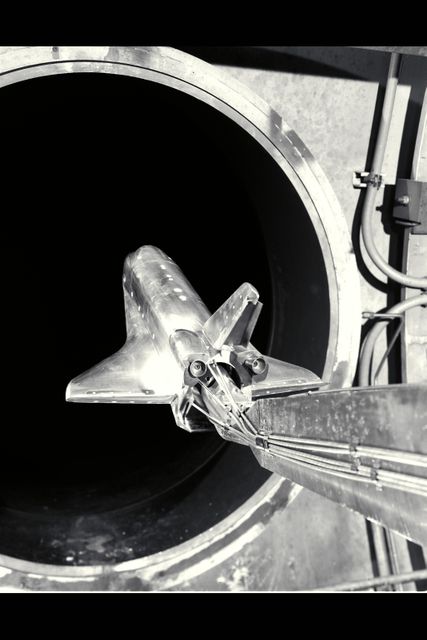 This image shows a scale model of a space shuttle undergoing aerodynamic testing in a 3.5ft hypersonic wind tunnel. The setting is a specialized aerospace testing facility used for examining spacecraft design and performance. Ideal for use in articles related to aerospace engineering, space exploration, and technological advancements in vessel design and testing methodologies.