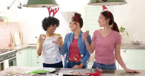 Friends decorating holiday cookies in bright kitchen laughing, tasting and celebrating