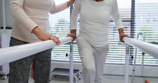 Senior woman practicing exercises with therapist's assistance in rehabilitation center. Useful for content related to elderly care, physical therapy, healthcare services, recovery process, and supporter roles in medical settings.