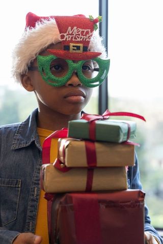 African american child holding christmas gifts wearing santa hat and green glitter glasses